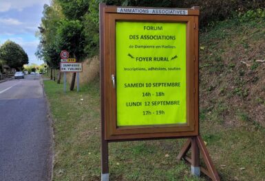 Un panneau d'affichage associatif contenant une annonce du forum des associations, deant panneau d'entrée de village
